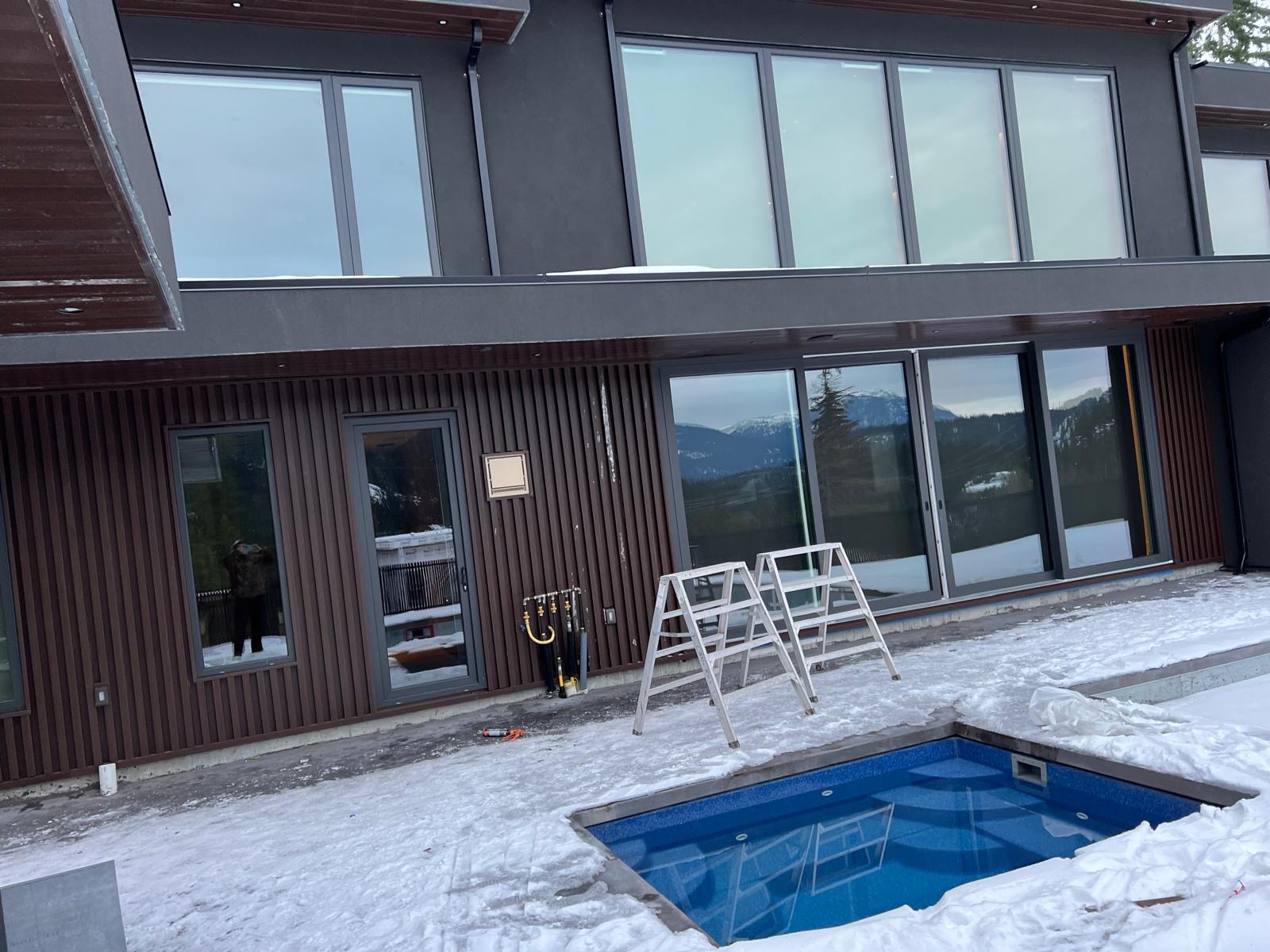 Mountain-side home with vertical brown siding, large windows and a pool